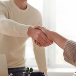 Close-up of professionals shaking hands over coffee in a modern office.